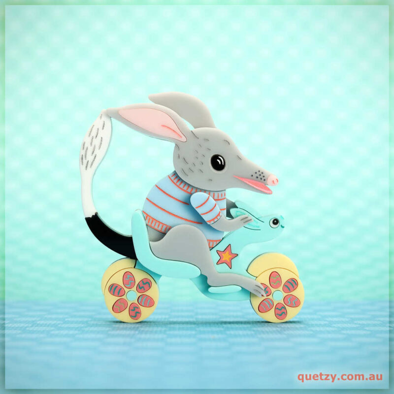 Stunning brooch of a Bilby riding a toy bike in beautiful pastel hues